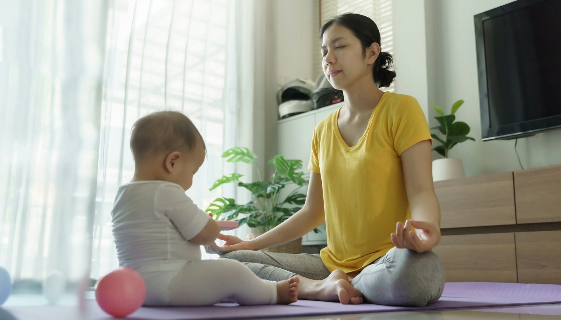 mother practicing mindfulness, child sits on exercise mat beside her